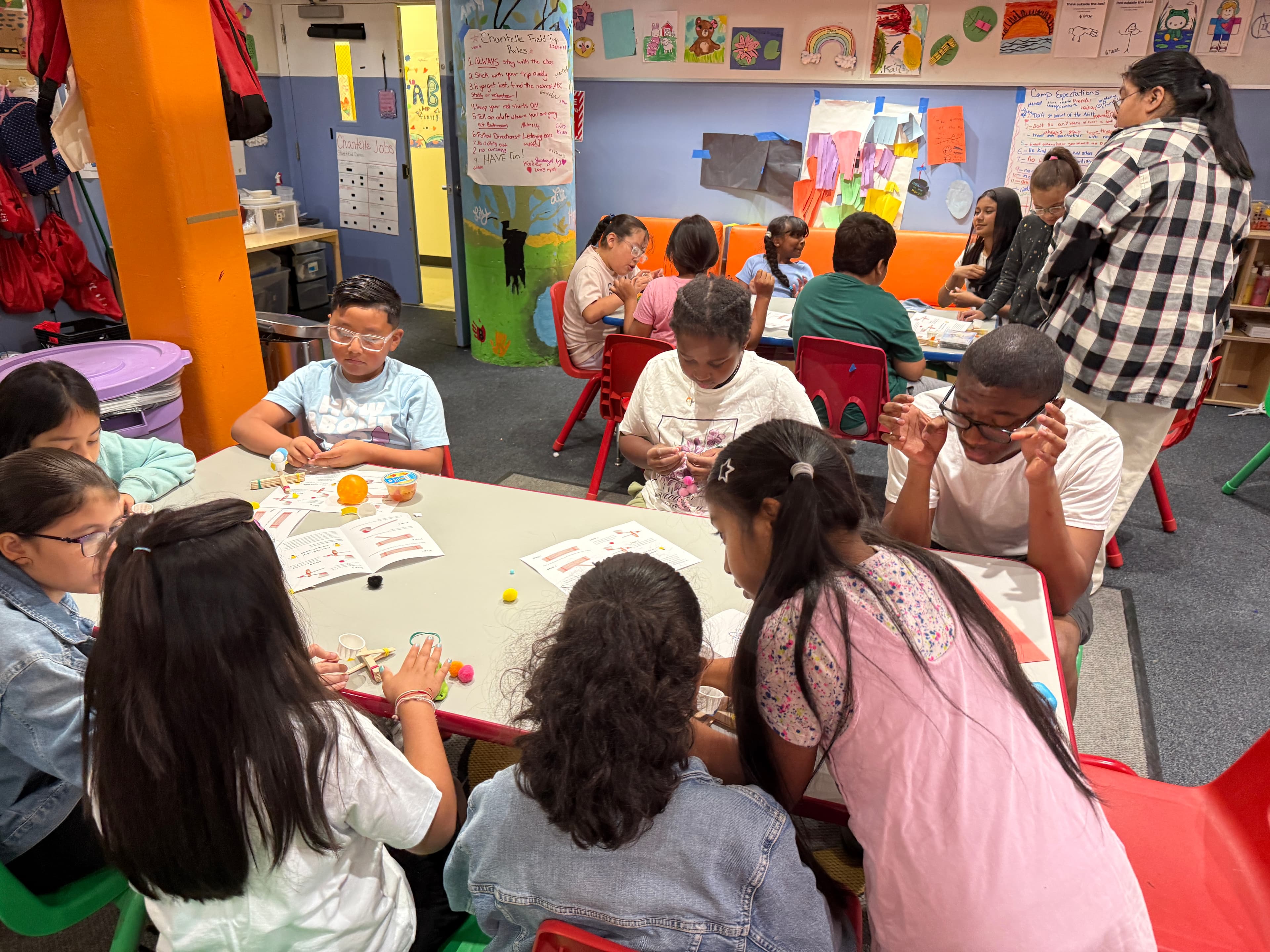 A full classroom of students at ABC working on their catapults, with staff and volunteers moving between the tables