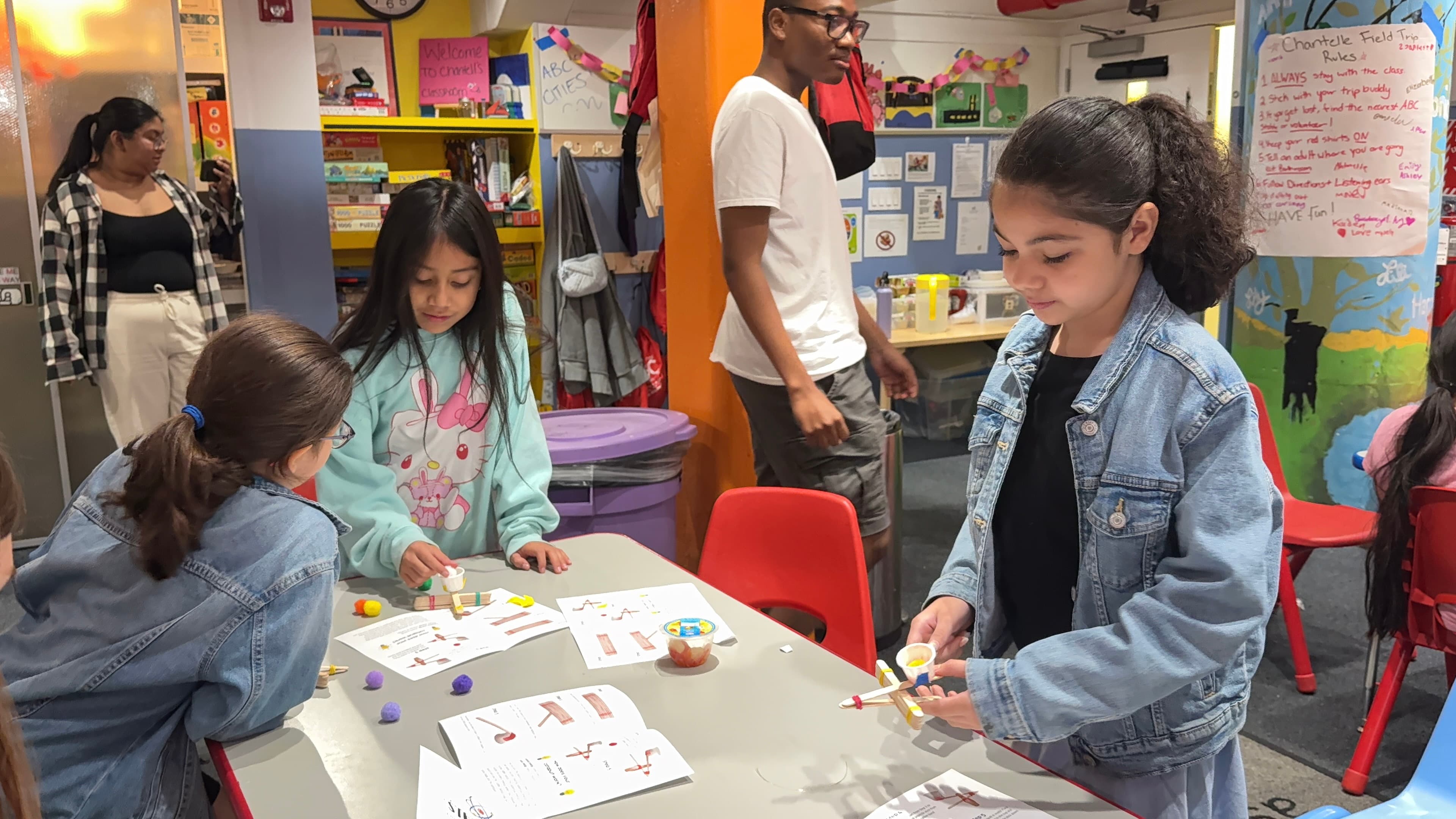 Three students following the printed instructions to assemble catapults from popsicle sticks, rubber bands and paper cups