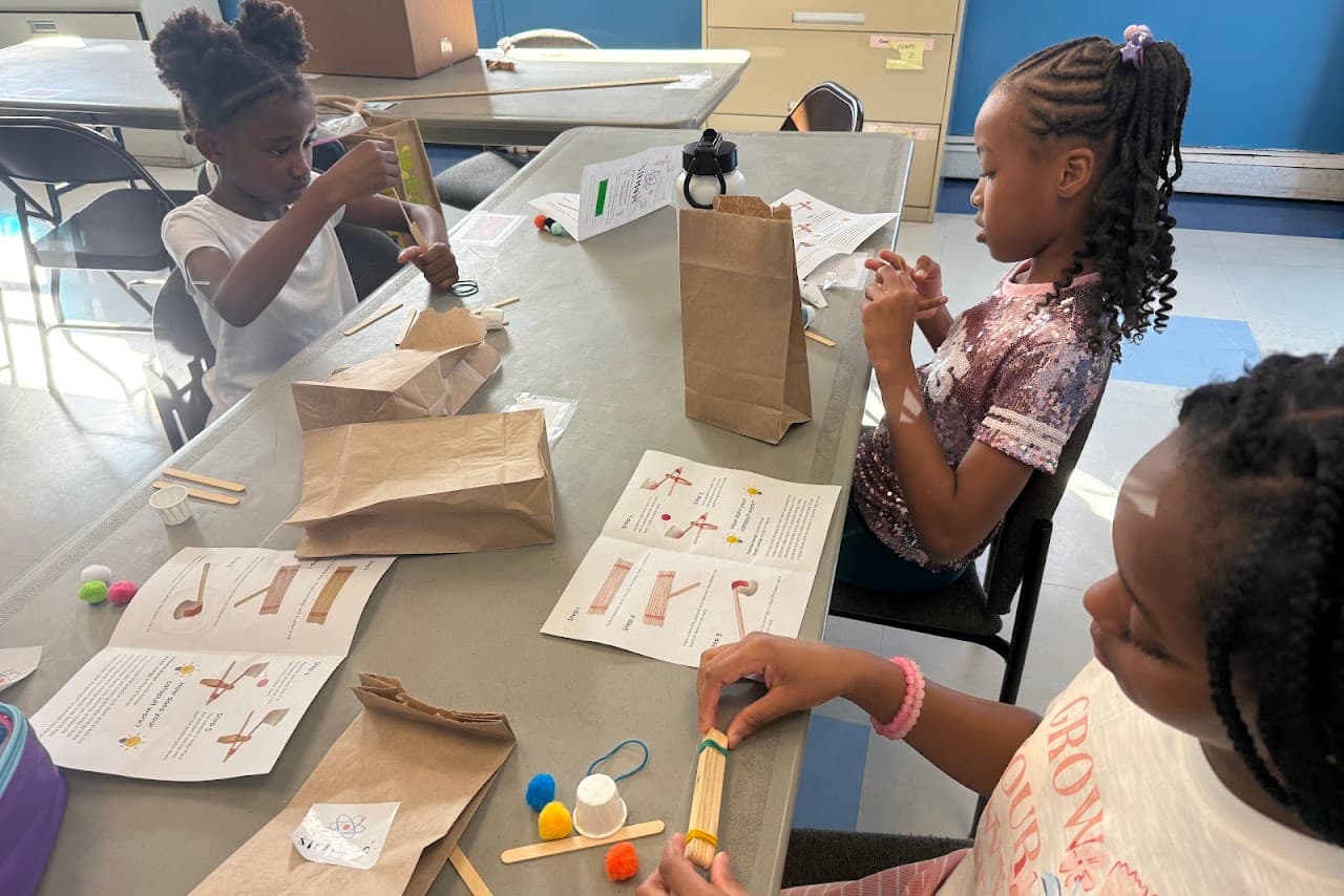 Three students assembling popsicle stick catapults at a table, following the illustrated instruction booklets